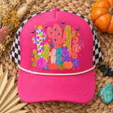 Whimsical folk-art cactus garden DTF transfer with polka dot, heart, and striped cacti, succulents, a striped pumpkin, bright flowers, stars, and black bats Shown on a fuchsia pink front panel with a cream rope and black-and-white checkered mesh back trucker hat.