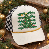 Hand-illustrated Christmas tree DTF transfer with glowing string lights, colorful ornaments, a gold star topper, pine branches, and scattered gold, teal, and red stars Shown on a cream front panel, gold rope, black-and-white checkered mesh back trucker hat.