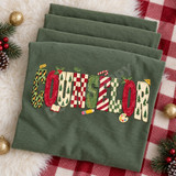 COUNSELOR Christmas word art DTF transfer in painterly block letters with leopard print, candy cane stripes, checkerboard and tree patterns, accented with holly, a pencil, an open book and a paint palette Shown on a Moss t-shirt.