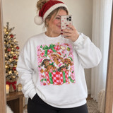 Dachshund puppies in Santa hats peeking out of a red and green checkered Christmas gift box with candy canes, cookies, and ornaments on a pink striped background DTF transfer Shown on a White crewneck sweatshirt.