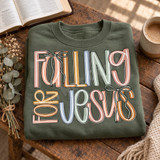 Falling for Jesus DTF transfer in bold hand-lettered multicolor typography with pastel blush, mustard, dusty blue, and sage tones, accented with sage green bow ribbons Shown on a Military Green crewneck sweatshirt.