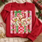 Whimsical Christmas ducks DTF transfer featuring five fluffy ducks in Santa hats and scarves popping out of a checkered gift box with candy canes and holly Shown on a Red crewneck sweatshirt.