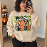 Fall pumpkin DTF transfer with a large orange pumpkin topped by a black-and-white striped bow, surrounded by checkerboard, star-print, and bat-print pumpkins and black stars on a green polka-dot background Shown on a Sand crewneck sweatshirt.