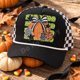 Fall pumpkin DTF transfer with a large orange pumpkin topped by a black-and-white striped bow, surrounded by checkerboard, star-print, and bat-print pumpkins and black stars on a green polka-dot background Shown on a Black front panel and bill with a white rope accent and black-and-white checkered mesh back trucker hat.