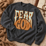 Fear God DTF transfer in bold gothic-western lettering with cracked texture, mint and tan colors, and heavy orange outlines on a black shirt Shown on a Dark Heather crewneck sweatshirt.