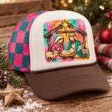 Folk-art nativity scene DTF transfer with Mary, Joseph, baby Jesus, sheep and donkey in a wooden stable under the Star of Bethlehem, on a splattered pink, orange and teal background with snowflakes Shown on a ivory front panel with brown bill and pink/teal checkered mesh trucker hat.