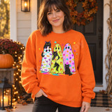 Three black cats with bat print, candy corn print, and polka dot ghost costumes surrounded by colorful stars DTF transfer design Shown on a Orange crewneck sweatshirt.