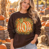 Watercolor-style pumpkin DTF transfer with orange, mint, peach, and gold stripes, gilded outlines, and a confetti-like dot splash background on a blue shirt Shown on a Dark Chocolate crewneck sweatshirt.