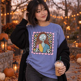 Blue-skinned ragdoll girl Halloween DTF transfer with auburn hair and patchwork top in a checkered frame with pink scalloped border and gold stars Shown on a Periwinkle t-shirt.