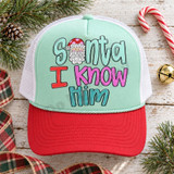 Santa I Know Him Christmas DTF transfer with hand-drawn Santa face replacing the letter A in bold mixed-color bubble lettering Shown on a mint front panel with red bill and white mesh back trucker hat.