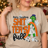 Merry Christmas Shitter's Full DTF transfer with grumpy green Christmas character dragging an orange hose in front of snowflakes Shown on a Sandstone t-shirt.