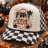 Spooky Season DTF transfer with distressed black lettering over an orange and cream striped ghost silhouette, surrounded by stars on a black polka-dot background Shown on a cream front panel, black rope, black-and-white checkered mesh back trucker hat.