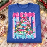 All Booked for Christmas DTF transfer with a whimsical book-stack Christmas tree, pine garland, fairy lights, and pink bubble lettering on a striped polka-dot background Shown on a Heather Deep Royal crewneck sweatshirt.