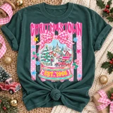Christmas Town snow globe DTF transfer with pink gingham bow, candy stripes, snowy village scene, red pickup truck, and Est. 1998 banner Shown on a Blue Spruce t-shirt.