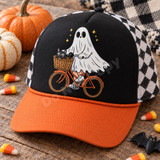 Cartoon ghost riding an orange bicycle with a black cat in the front basket and yellow sparkle stars, DTF transfer on a yellow t-shirt Shown on a Black front panel, burnt orange bill, black and white checkered mesh back trucker hat.