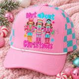 Nut About Christmas DTF transfer featuring three whimsical pink and turquoise nutcracker soldiers with crowns, a drum, candy cane, and tiny Christmas tree on pink polka-dot stripes Shown on a bubblegum pink front panel with white rope and a pink-and-teal checkered mesh back trucker hat.
