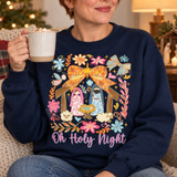Oh Holy Night nativity DTF transfer with Mary, Joseph, baby Jesus, angel and sheep framed by an orange floral bow, gold star and pastel flowers, pink script lettering below Shown on a Navy crewneck sweatshirt.
