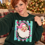 Vintage-style Santa Claus face DTF transfer with pink hat and holly, framed in a scalloped pink and teal oval border with snowflakes and stars Shown on a Fan Dark Green crewneck sweatshirt.
