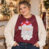 Whimsical Santa face DTF transfer with red polka-dot hat, curly white hair and beard, and pink cheeks in hand-drawn line art style Shown on a Wine t-shirt.