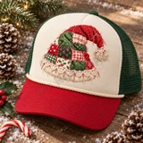 Quilted patchwork Santa hat DTF transfer with red and green holiday-print fabric squares, crosshatch stitching, crocheted lace trim, and a chunky pom-pom tassel Shown on a Cream front panel / crimson red bill / forest green mesh trucker hat.