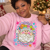 Whimsical Santa face DTF transfer with dotted fur trim, swirly beard, and patchwork hat inside a pink and teal scalloped frame Shown on a Light Pink crewneck sweatshirt.