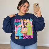Jesus is the Reason for the Season nativity DTF transfer with pastel Mary and Joseph kneeling beside baby Jesus, pink striped polka-dot background, and colorful stars Shown on a Indigo Blue crewneck sweatshirt.