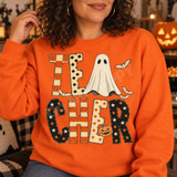 TEACHER Halloween DTF transfer in patchwork block letters with checkerboard, stripes, polka dots and stars, featuring a ghost, jack-o'-lantern, and bats Shown on a Orange crewneck sweatshirt.