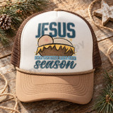 JESUS the reason for the season Christmas DTF transfer with hand-drawn nativity manger scene featuring a swaddled baby peeking over straw bedding Shown on a ivory front panel with tan rope and warm brown mesh back trucker hat.