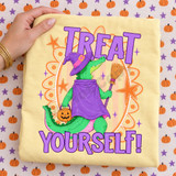 Treat Yourself Halloween DTF transfer with a green alligator dressed as a witch in a purple hat and cloak, holding a broom and jack-o-lantern pail, framed by orange stars on a retro striped background Shown on a Butter t-shirt.
