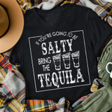 If You're Going To Be Salty Bring The Tequila WHITE Screen Print Heat Transfer, black t-shirt with a humorous tequila-themed design, surrounded by outdoor accessories.