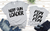 Nerf Gun Loader Screen Print Heat Transfer, gray T-shirts with bold black text design, laid on a white wooden surface with denim jeans.