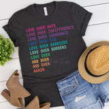 Love Over Hate Love Over Indifference Screen Print Heat Transfer T-shirt, dark gray T-shirt with colorful text design displayed alongside tan hat, denim shorts, and brown heeled boots on a white wooden background.