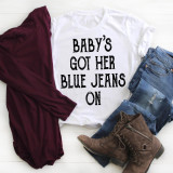 Baby's got her blue jeans on country music sublimation transfer, white t-shirt with black text, denim jeans, brown boots, maroon sweater, on a white wooden surface.