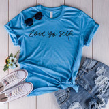 Love Yo Self Screen Print Transfer, blue T-shirt with black script lettering and casual denim shorts, with accessories like white sneakers, sunglasses, and a small bouquet of flowers.