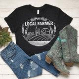 Support Your Local Farmer White Screen Print Transfer T-shirt, casual black t-shirt with a farm-themed design, distressed blue jeans, and cowboy boots with green and gray patterns, on a white wooden background.
