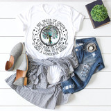 What a Wonderful World Earth Day Sublimation Transfer T-shirt with a colorful tree design, paired with ripped jeans, gray slip-on shoes, a striped shirt tied around the waist, and a plant in a black book, laid out on a white wooden background.