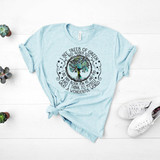 I See Trees of Green Screen Print Heat Transfer, a light blue T-shirt with a circular tree graphic and poetic text about trees and blooming, laid flat on a white wooden surface with small potted succulents and white sneakers nearby.