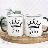 Queen Sublimation Transfer, two white mugs with black handles and rims featuring a crown graphic and the words "King" and "Queen" in black script, displayed on a wooden surface.