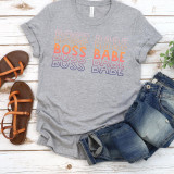 Boss Babe Screen Print Heat Transfer, colorful graphic t-shirt with 'Boss Babe' text in pink, orange, purple, and yellow colors laid out on a white wooden surface with denim jeans and brown sandals nearby.