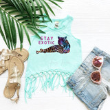 Stay Exotic FINAL STOCK - YOUTH Screen Print Heat Transfer, youth tank top with a colorful tiger and lion graphic and fringed hem, surrounded by casual summer accessories including sandals, sunglasses, and denim shorts on a white wooden surface.