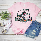 Teaching is a Walk in the Park Screen Print Heat Transfer, pink t-shirt with tropical leaf and floral design and text, casual denim shorts, white sneakers, green plant on white wooden background.