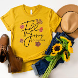 Fall for Jesus He Never Leaves Screen Print Transfer, yellow t-shirt with fall leaves design and inspirational message, paired with brown boots, denim jeans, beige hat, and a bouquet of sunflowers.