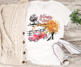 Autumn Vibes Sublimation Transfer, a colorful t-shirt with fall-themed design including a red truck, autumn trees, and the words 'Autumn Vibes' displayed on a wooden background with sneakers, a knitted cardigan, and a plant nearby.