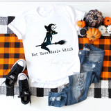 Not Your Basic Witch Sublimation Transfer T-shirt featuring a witch silhouette with starry night design and text, displayed alongside sneakers, jeans, and Halloween decorations on a plaid tablecloth.