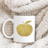 Golden Apple Sublimation Transfer, metallic gold apple design on white ceramic mug placed on soft plush fabric.
