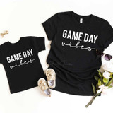 Game Day Vibes White Youth Screen Print Transfer, black t-shirts for kids with 'Game Day Vibes' design, matching adult and child shirts, stylish children's sneakers, and a bouquet of flowers for a sporty family look.