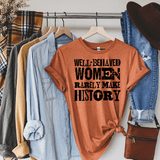 Well-Behaved Women Rarely Make History Screen Print Heat Transfer T-shirt, orange casual tee with bold black text, displayed among jeans, shirts, a hat, and a purse.