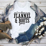 Ain't No Shame In My Flannel And Boots Game Sublimation Transfer, white t-shirt with black text, casual fashion style with plaid shirt, jeans, and cowboy boots, laid out on a wooden background with cotton branches for a rustic look.