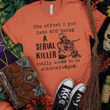 The Effort I Put Into Not Being a Serial Killer Screen Print Transfer T-shirt, orange with black skull and text design.