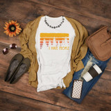 I Hate People Sublimation Transfer, white T-shirt with a sunset and tree design and the text I Hate People, surrounded by everyday accessories on a wooden surface.